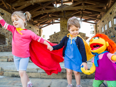 Muppet Julia plays with two young girls wearing capes.