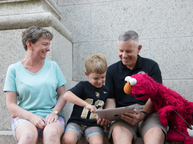 A young boy plays on a tablet with his parents and with Elmo.