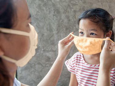 A parent putting a protective face mask on a child.