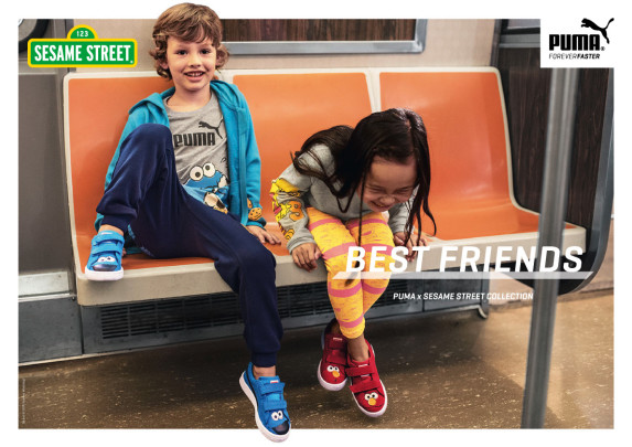 Two children sit on a bench inside of a New York City subway train. They're laughing and wearing Sesame street branded clothing.