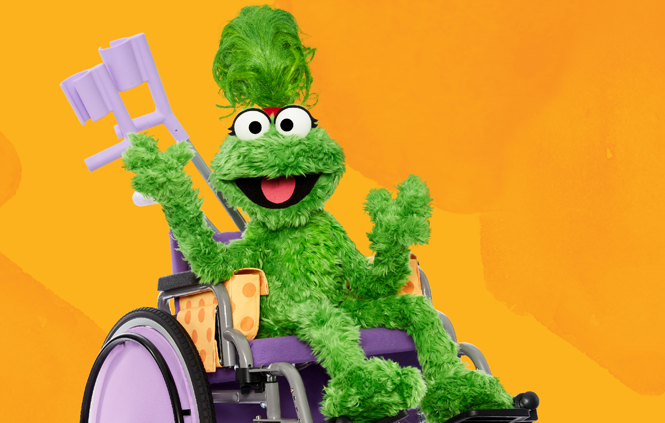 Ameera, a green muppet from Ahlan simsim, poses happily in her wheelchair