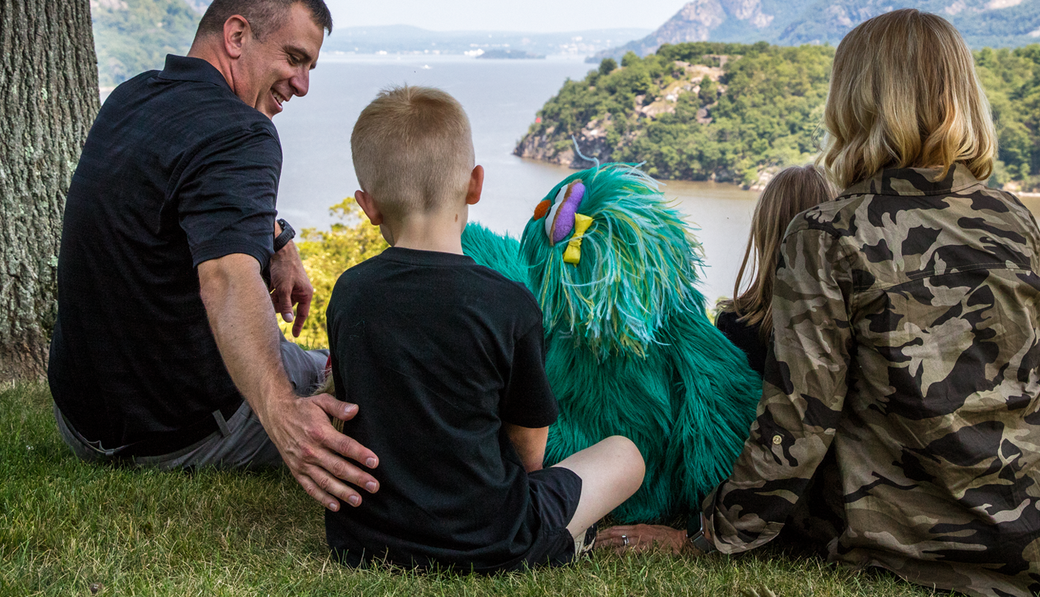 Rosita sits with a young boy and his parents on a hilltop overlooking water.