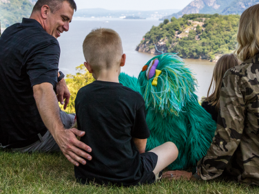 Rosita sits with a young boy and his parents on a hilltop overlooking water.