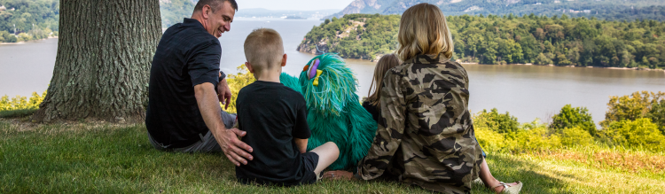 Rosita sits with a young boy and his parents on a hilltop overlooking water.