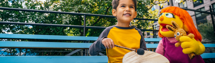 Julia smiles with her bunny as she sits with a young boy playing a drum.