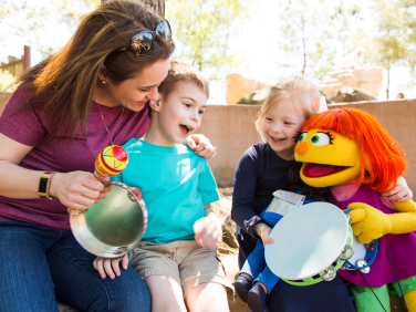 Muppet Julia plays different musical instruments with two children and their mother.