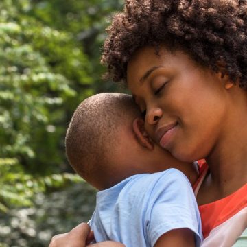 A mom calmly embraces her young child with a hug.