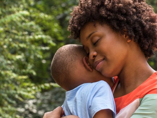 A mom calmly embraces her young child with a hug.