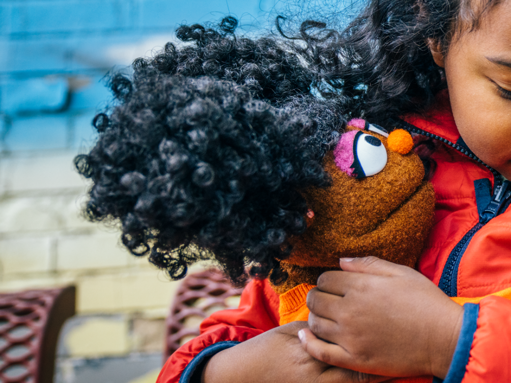 Gabrielle, the muppet, gives a young girl a big hug.