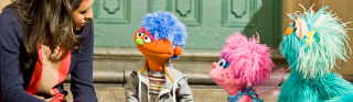 A visibly upset muppet boy is comforted by an adult woman, Abby Cadabby, and Rosita.