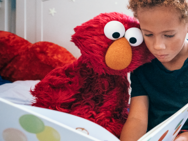 Elmo and a child read a book together.