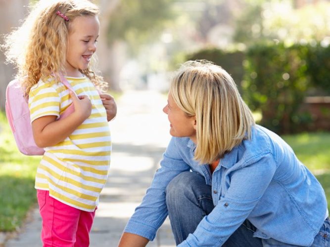 A mother tying her daughter's shoelace on the sidewalk.