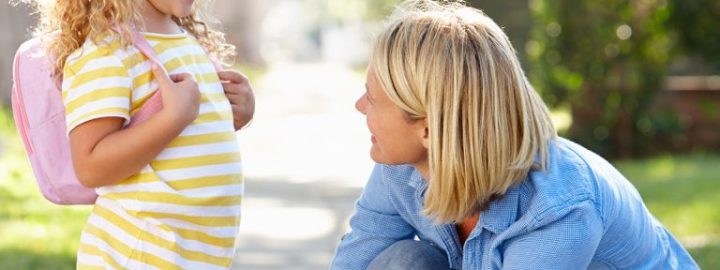 A parent tying their child's shoelace on the sidewalk.