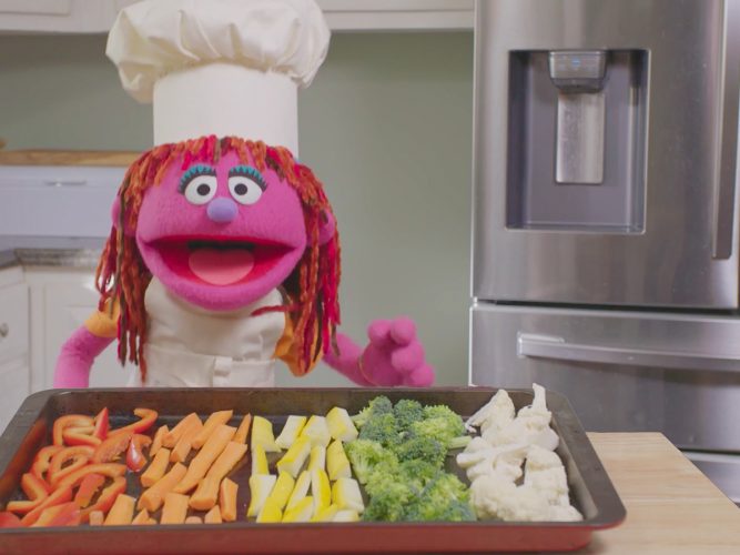 Lily in a chef's hat with a tray of vegetables.