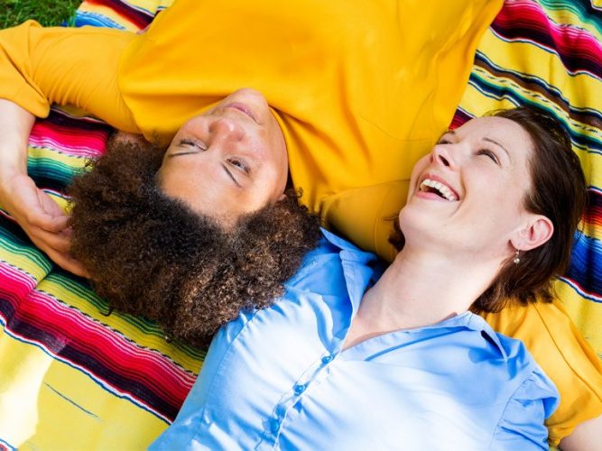 Two moms laying on a blanket in a park.