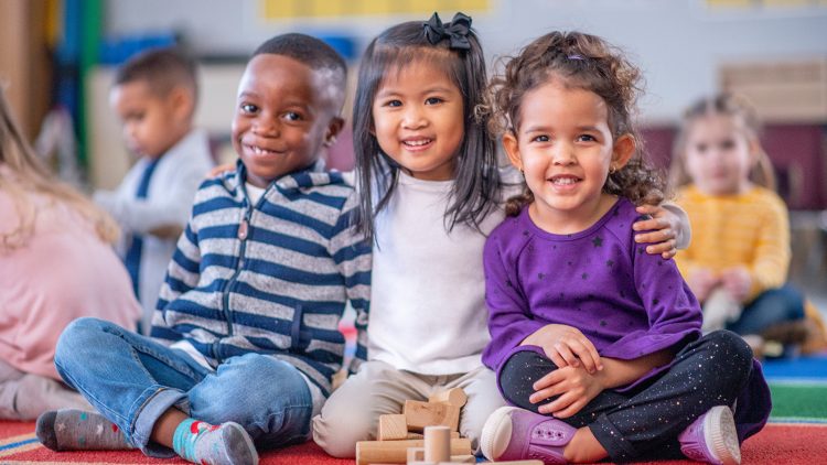 Three young kids smiling and playing with blocks in class.