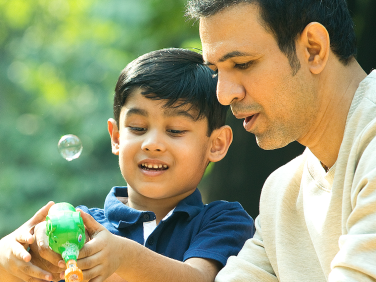 A father helps his son blow bubbles.