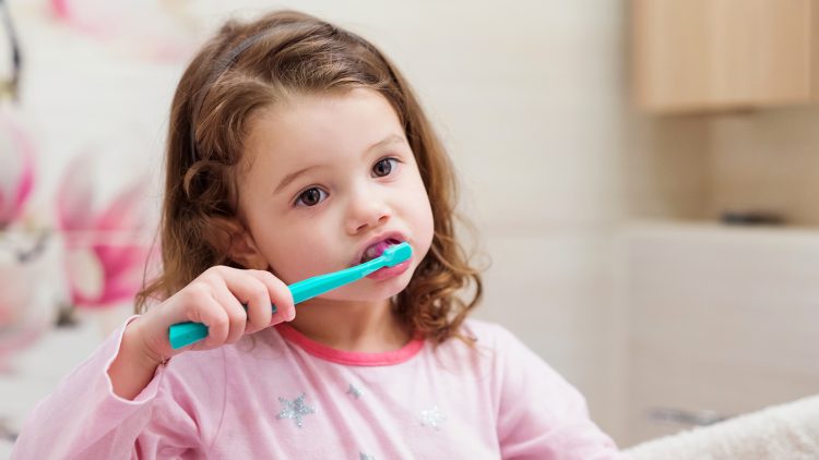 A little girl brushing her teeth in the bathroom.