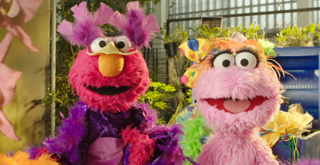 Elmo and Lola, a pink Muppet from Plaza Sésamo, are dressed up in costumes and playing pretend!
