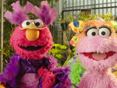 Elmo and Lola, a pink Muppet from Plaza Sésamo, are dressed up in costumes and playing pretend!