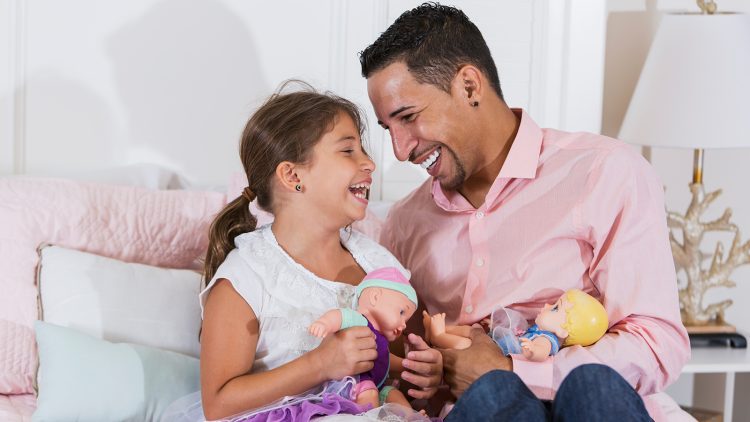 Father and young daughter laugh together, playing with dolls.