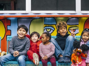 A large group of kids sitting in front of a mural.