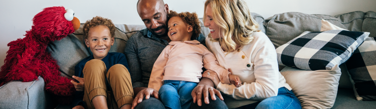 A family on the couch laughing with Elmo.