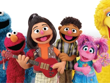 Ji-Young poses with her red guitar alongside Cookie Monster, Elmo, Tamir, Abby, and Big Bird.