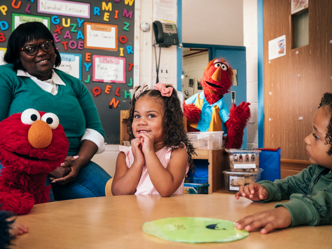 Elmo and his dad talking with a teacher and students.