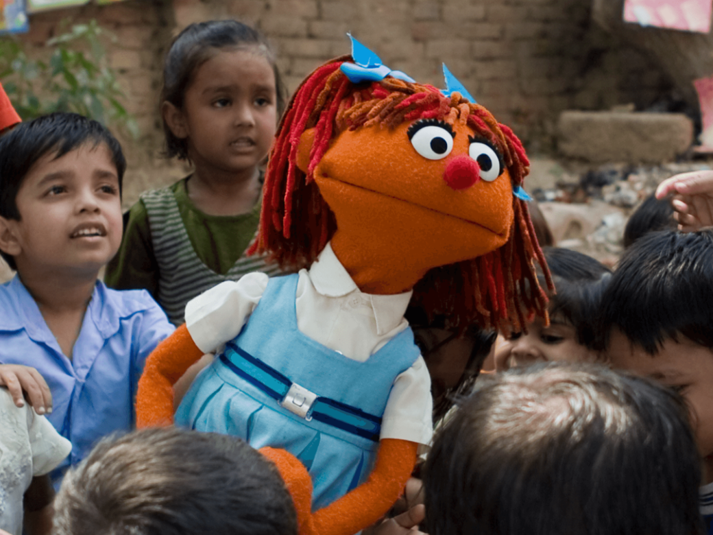 A young muppet girl poses amongst a group of children.