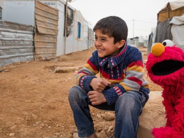 Elmo and little boy sitting outside.