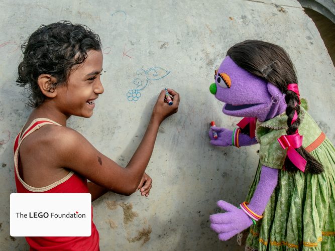 A muppet of Sesame Street and young girl coloring.