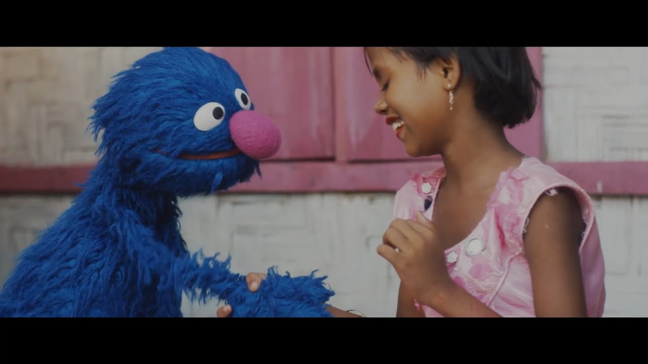 Grover holds the hand of a young child.