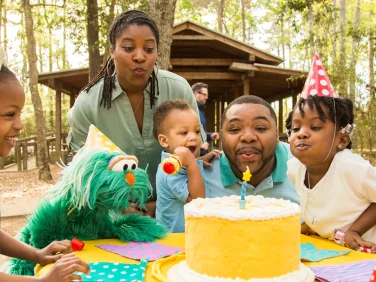 Two grownups, two children, and Rosita blow out a candle on a birthday cake.