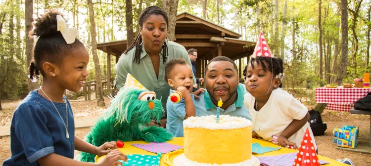 Two grownups, two children, and Rosita blow out a candle on a birthday cake.