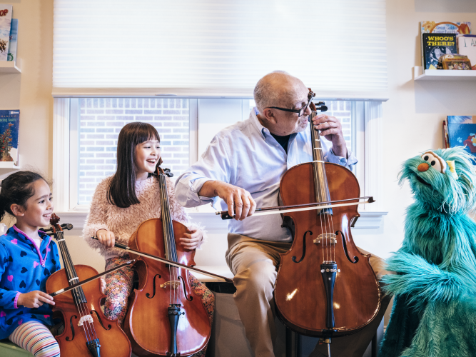 Rosita looks on as a grown up and two kids learn to play the cello.