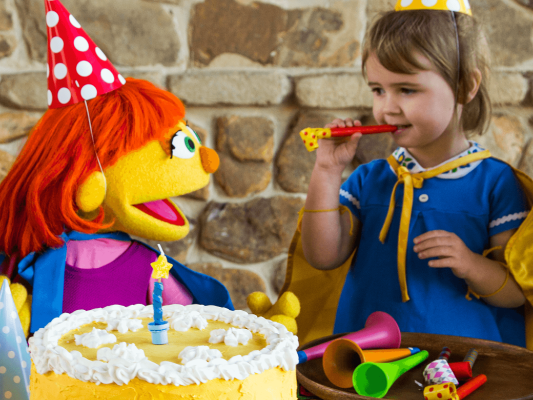 A mother, father, two girls, and Julia wear party hats and celebrate with a cake.