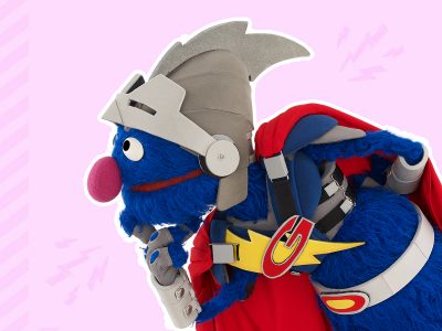 Super Grover, dressed in a helmet and cape, rests his chin in his hands and thinks.