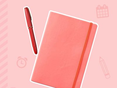 A pink notebook lays next to a pink pen.