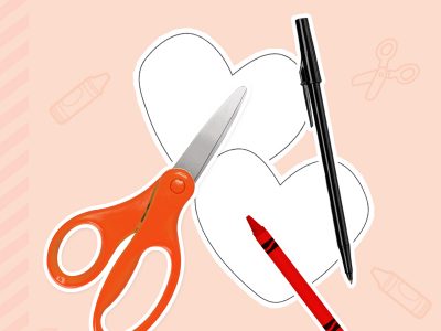 A pair of scissors lays next to two paper hearts, a pen, and a crayon.
