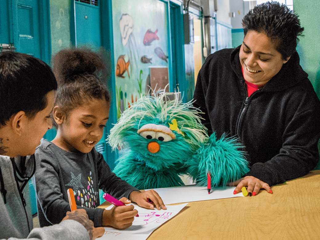 Rosita and a young girl draw together with two adults in school.