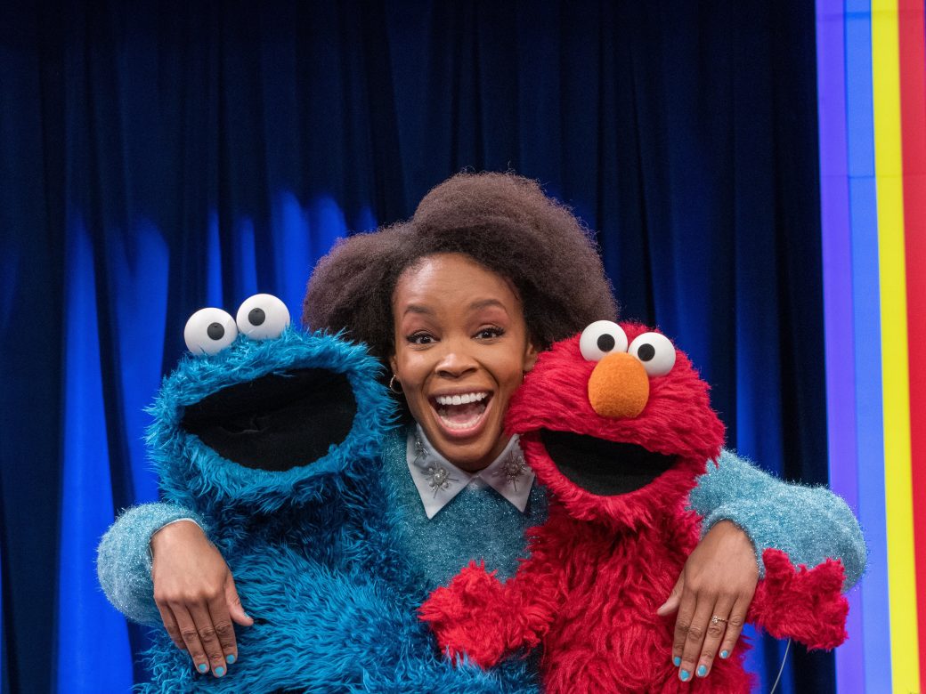 An adult poses with Cookie Monster and Elmo
