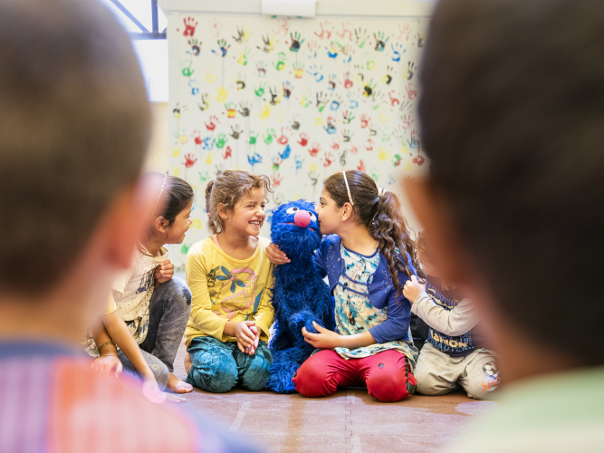 Children sit happily in a circle with Grover