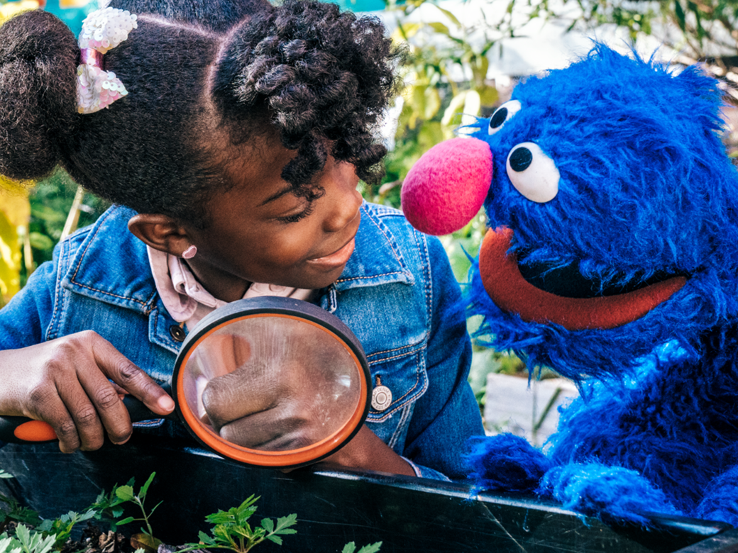 A child and Grover looking through a magnifying glass.