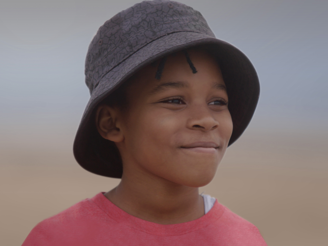 A child stands on a beach wearing a bucket hat and a red shirt
