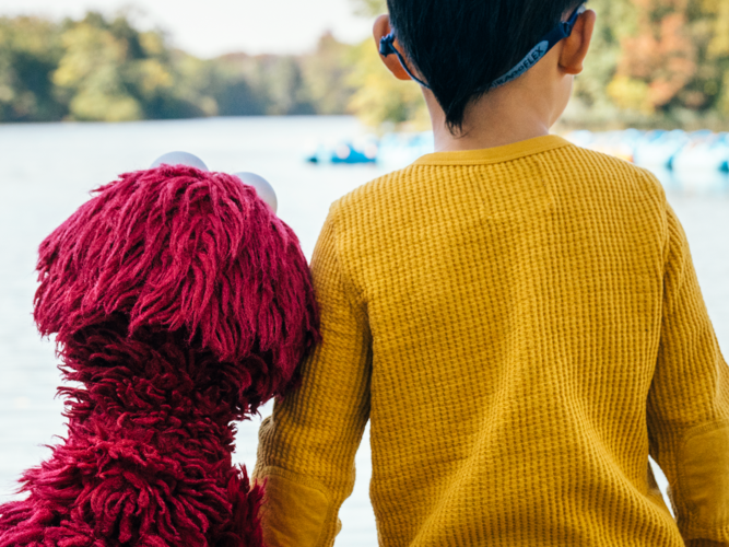 Elmo and child looking out at a lake.