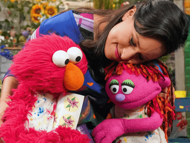 A woman gives Elmo and another muppet, Lily, a big hug.Lily is faced with some traumatic experiences.
