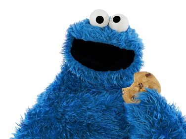 Cookie Monster's mouth hangs open and he holds a cookie in his left hand.