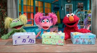 Karli, Abby, and Elmo stand behind their own shoe boxes, wrapped in colorful paper and decorations.