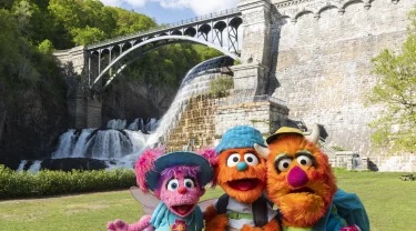 Abby Cadabby, Rudy, and Freddie pose in front of a bridge and waterfall